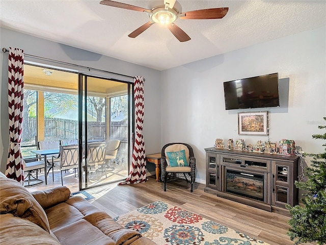 living room featuring baseboards, a glass covered fireplace, ceiling fan, wood finished floors, and a textured ceiling