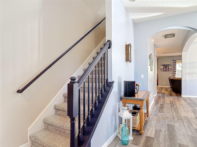 staircase featuring arched walkways, a textured ceiling, wood finished floors, and baseboards