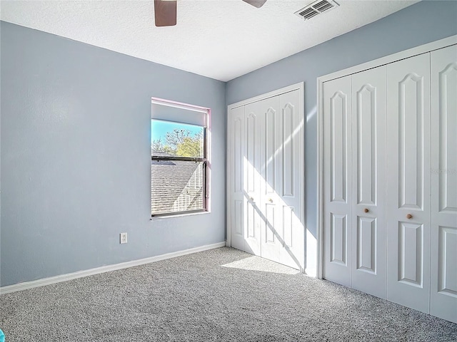 unfurnished bedroom featuring carpet, multiple closets, visible vents, a textured ceiling, and baseboards