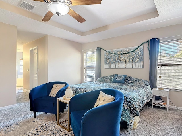 bedroom with carpet floors, a tray ceiling, visible vents, and baseboards