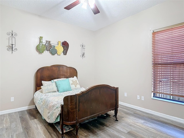 bedroom featuring a ceiling fan, a textured ceiling, baseboards, and wood finished floors