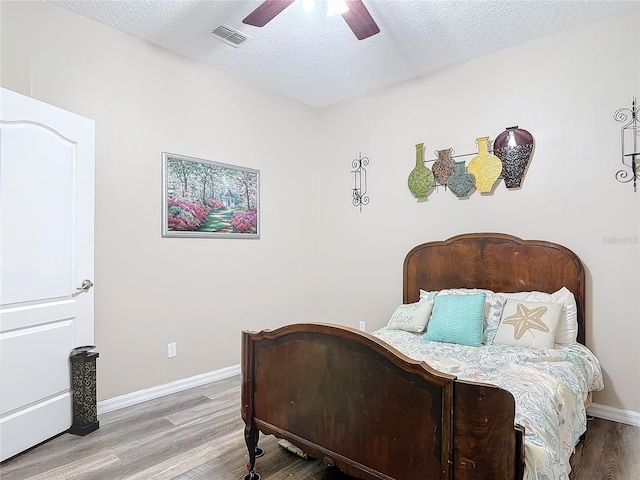 bedroom with visible vents, ceiling fan, a textured ceiling, wood finished floors, and baseboards