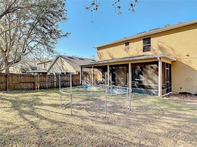 rear view of house featuring a sunroom, fence, a lawn, and stucco siding