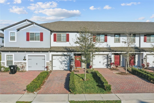 townhome / multi-family property with stone siding, driveway, an attached garage, and stucco siding