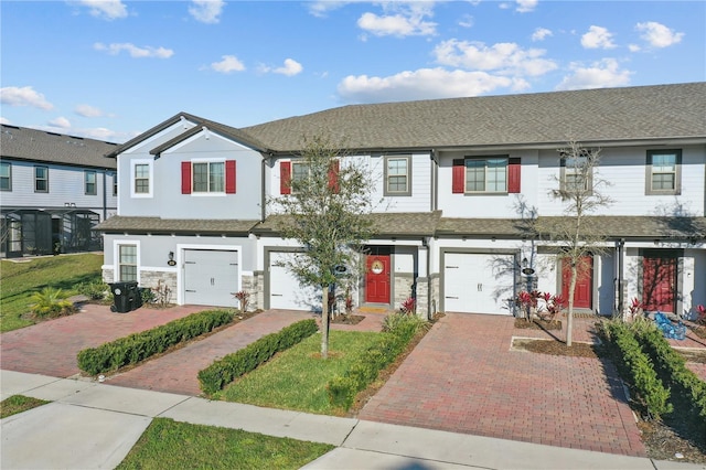 multi unit property with a garage, driveway, stone siding, and stucco siding