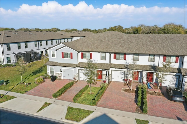 townhome / multi-family property featuring driveway, a garage, a residential view, a front lawn, and stucco siding