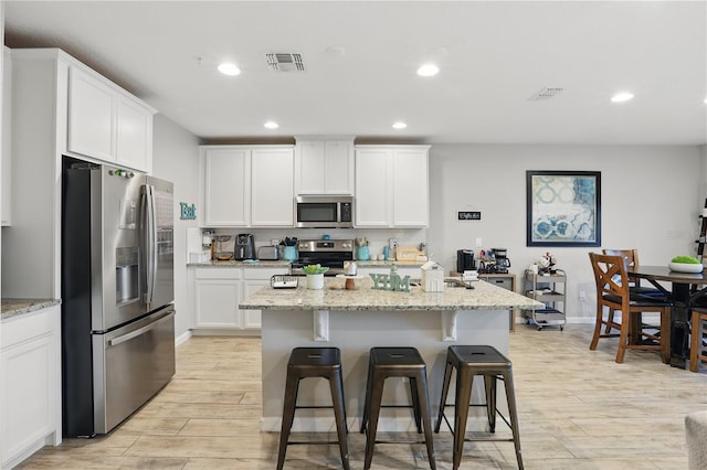 kitchen with a breakfast bar area, stainless steel appliances, visible vents, white cabinetry, and light wood-type flooring