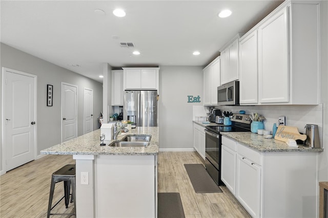 kitchen with a center island with sink, stainless steel appliances, visible vents, a sink, and light wood-type flooring