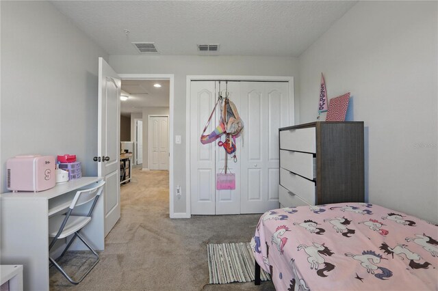 bedroom with a closet, light colored carpet, visible vents, and a textured ceiling