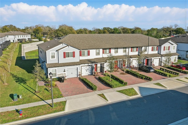 townhome / multi-family property featuring an attached garage, decorative driveway, a residential view, stucco siding, and a front lawn