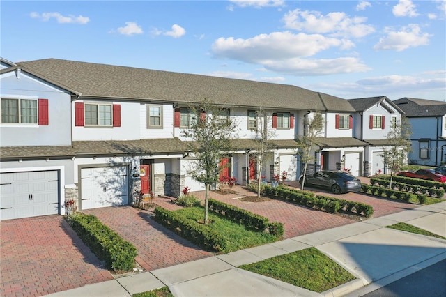 multi unit property with driveway, stone siding, a residential view, an attached garage, and stucco siding