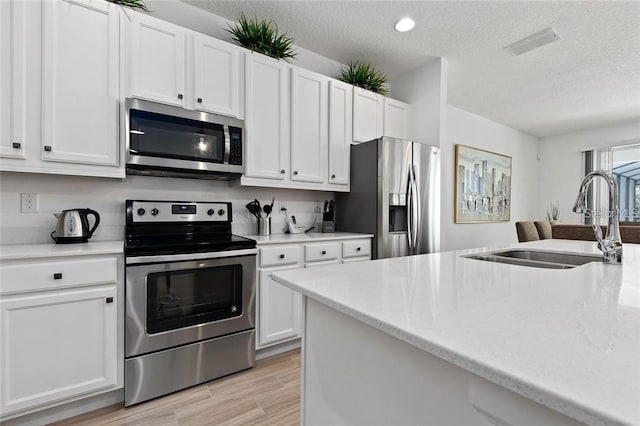 kitchen featuring stainless steel appliances, white cabinets, visible vents, and a sink