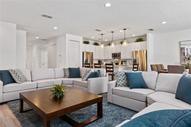 living room with light wood-style floors, visible vents, a textured ceiling, and recessed lighting