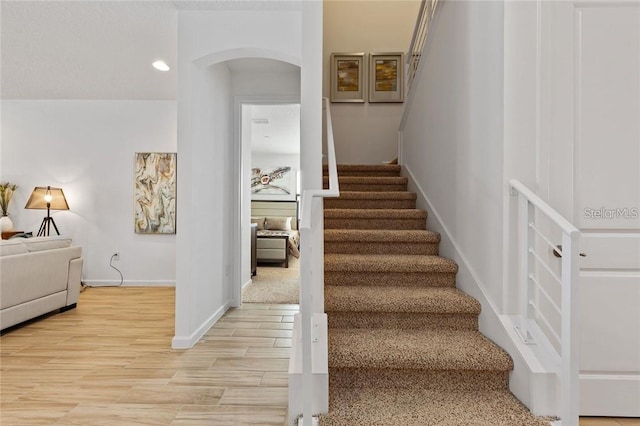 staircase with arched walkways, wood finished floors, and baseboards