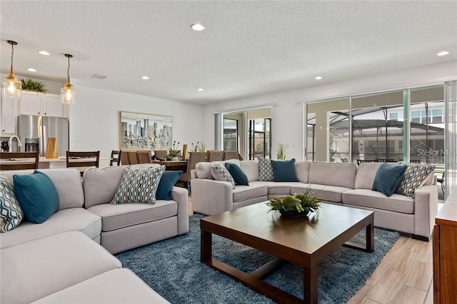 living area with light wood-type flooring, visible vents, a textured ceiling, and recessed lighting