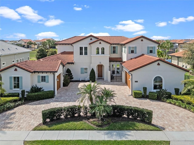 mediterranean / spanish-style home with a tile roof, a residential view, decorative driveway, and stucco siding