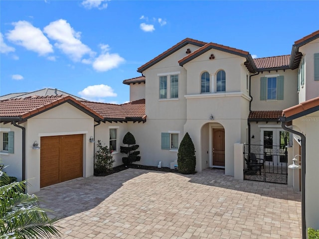 mediterranean / spanish-style home featuring a garage, driveway, a tiled roof, and stucco siding