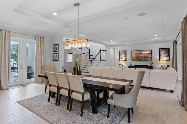 dining room with light wood-style flooring, stairs, french doors, ornamental molding, and a tray ceiling