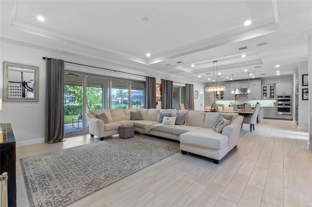 living room with ornamental molding, a tray ceiling, light wood-type flooring, and baseboards