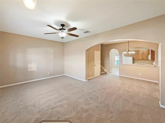 empty room featuring arched walkways, ceiling fan with notable chandelier, light carpet, baseboards, and stairs