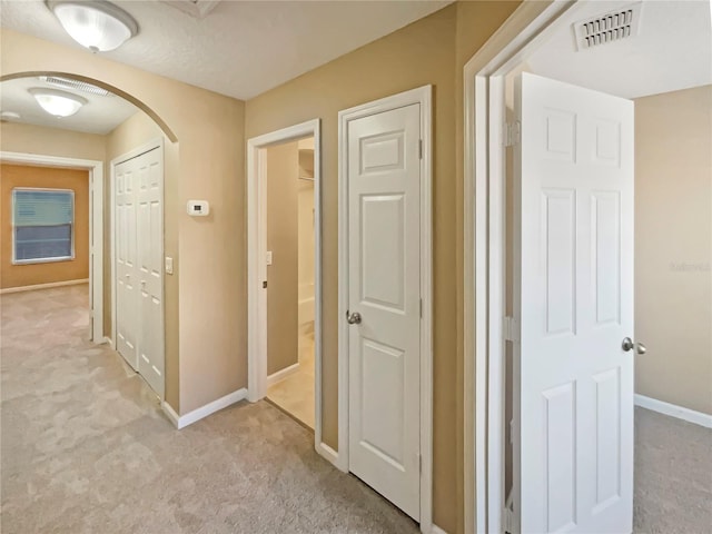 corridor featuring arched walkways, baseboards, visible vents, and light colored carpet