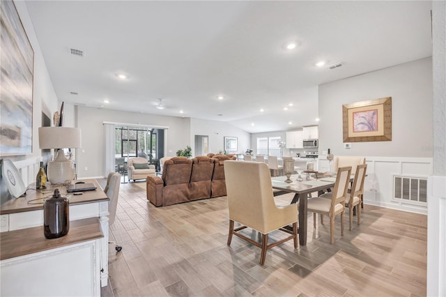 dining area with visible vents, light wood-type flooring, and vaulted ceiling