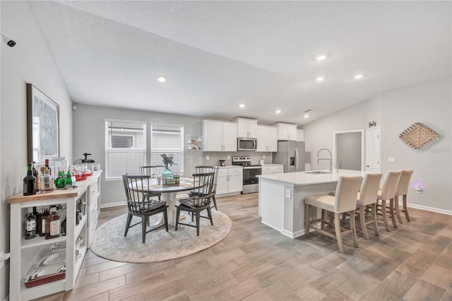 kitchen featuring light wood finished floors, a center island with sink, vaulted ceiling, stainless steel appliances, and a sink