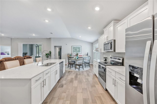 kitchen featuring lofted ceiling, a kitchen island with sink, a sink, stainless steel appliances, and white cabinets