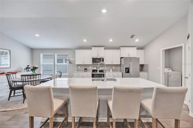 kitchen with white cabinetry, lofted ceiling, an island with sink, and appliances with stainless steel finishes