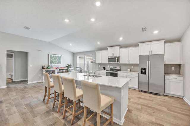 kitchen featuring visible vents, a kitchen bar, a sink, appliances with stainless steel finishes, and vaulted ceiling