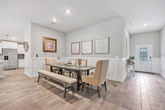 dining area featuring visible vents, light wood-type flooring, recessed lighting, wainscoting, and a decorative wall