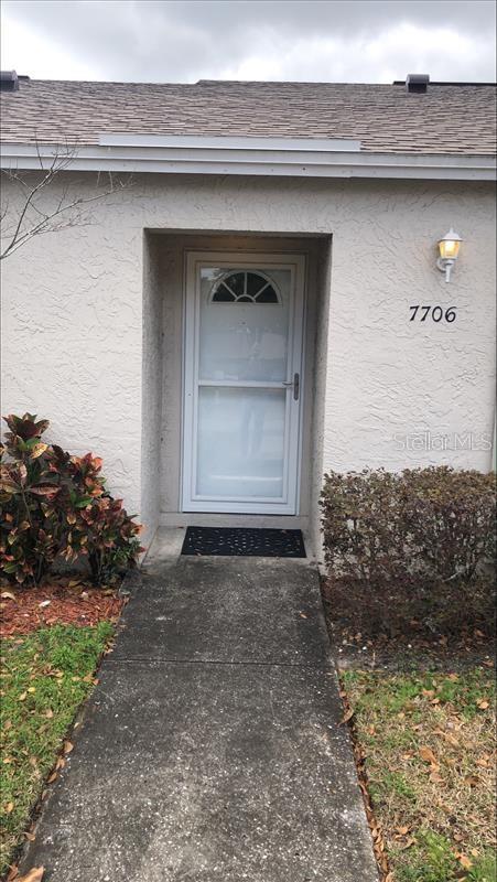 property entrance featuring roof with shingles and stucco siding