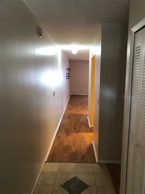 hallway featuring a textured ceiling, baseboards, and tile patterned floors