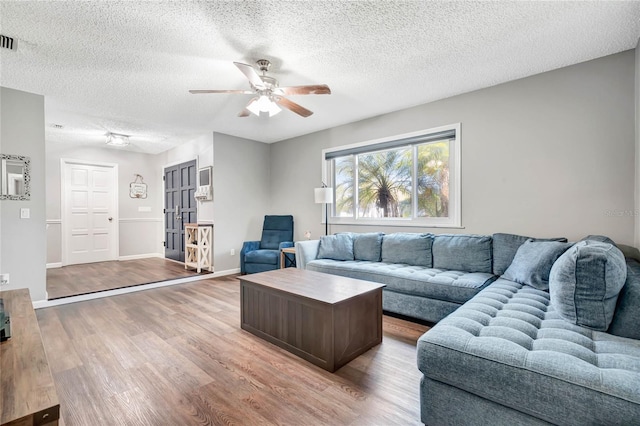 living room featuring a textured ceiling, ceiling fan, wood finished floors, visible vents, and baseboards