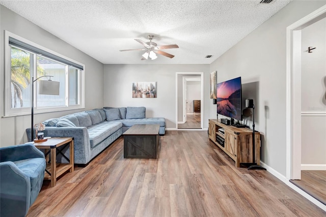 living room featuring light wood-style floors, a ceiling fan, baseboards, and a textured ceiling