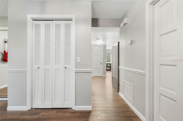 corridor with dark wood-style flooring, visible vents, a textured ceiling, and baseboards