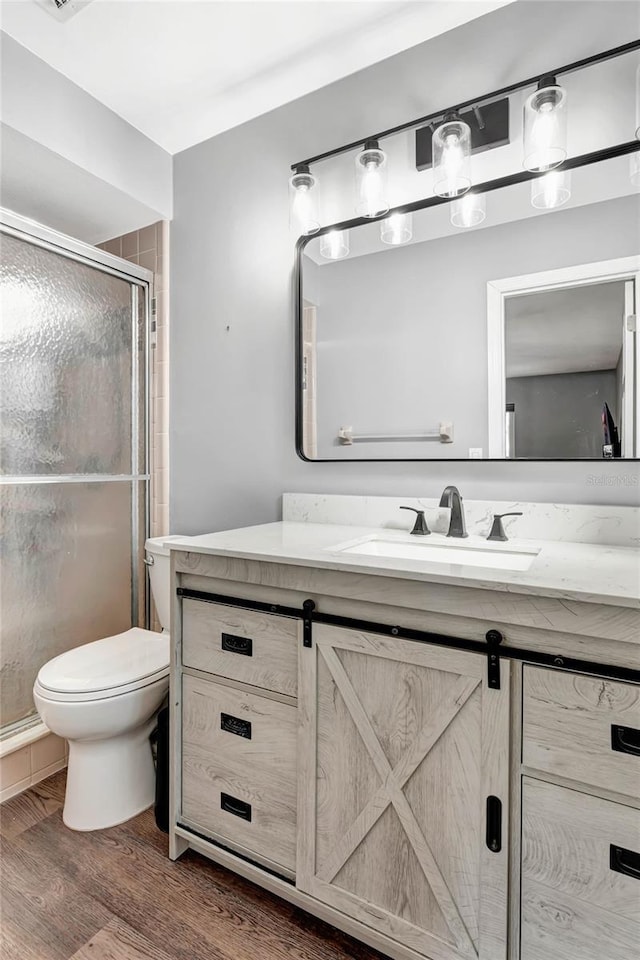 bathroom featuring toilet, a shower stall, wood finished floors, and vanity