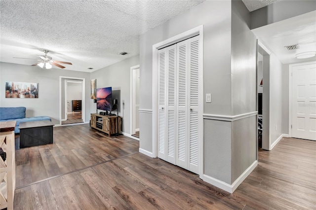 hallway with a textured ceiling, visible vents, and wood finished floors