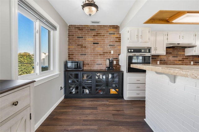 kitchen with stainless steel microwave, visible vents, white cabinets, black oven, and under cabinet range hood