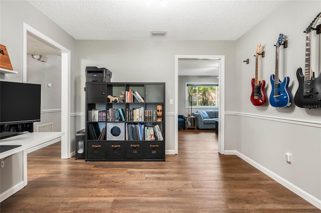 hallway with a textured ceiling, wood finished floors, visible vents, and baseboards