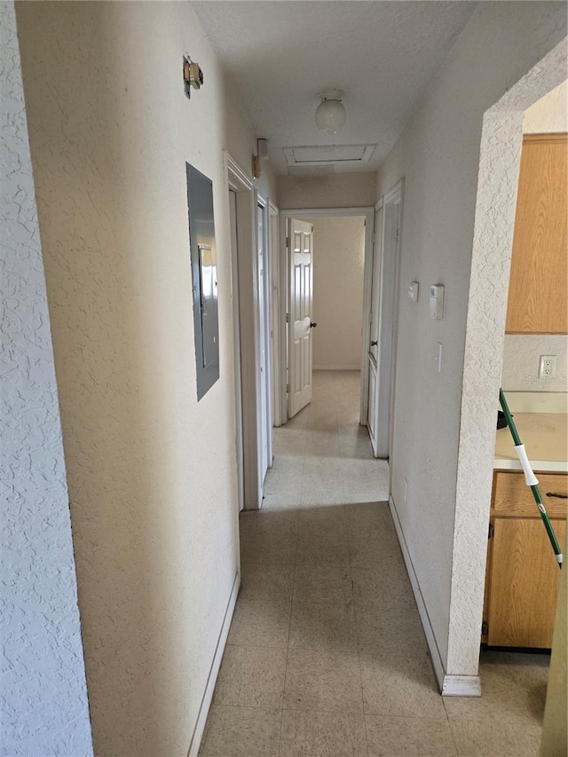 corridor with electric panel, attic access, baseboards, and a textured wall