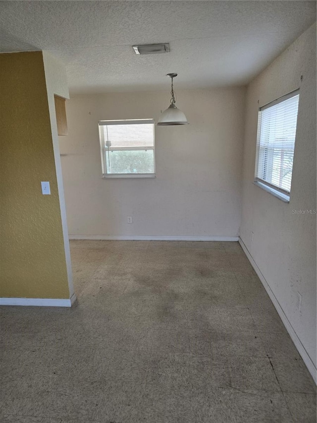 spare room with visible vents, a textured ceiling, baseboards, and a textured wall