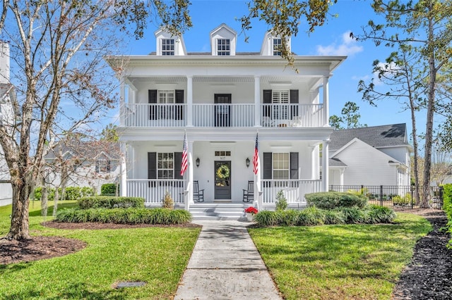 neoclassical home with a balcony, fence, a porch, and a front yard