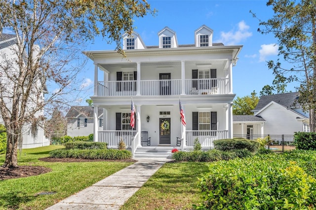 neoclassical home with stucco siding, covered porch, a front yard, fence, and a balcony