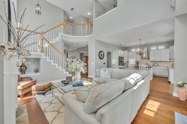 living area featuring arched walkways, stairway, light wood-style flooring, and a notable chandelier