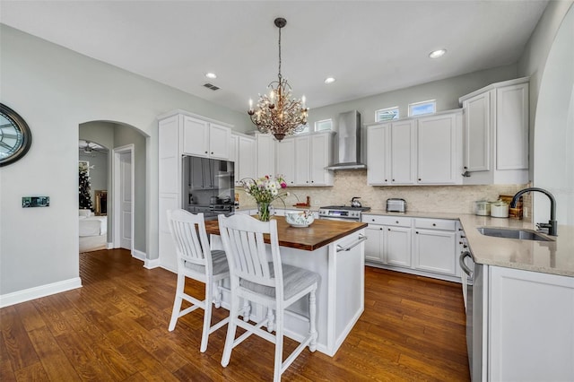 kitchen featuring arched walkways, appliances with stainless steel finishes, a sink, wood counters, and wall chimney exhaust hood