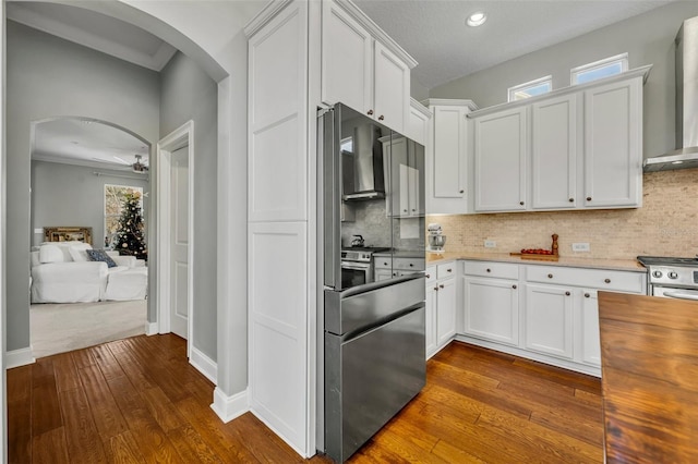 kitchen featuring dark wood-style floors, white cabinetry, arched walkways, and wall chimney range hood