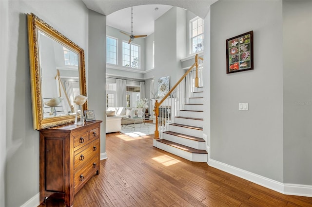 entryway with arched walkways, a towering ceiling, baseboards, stairway, and hardwood / wood-style floors