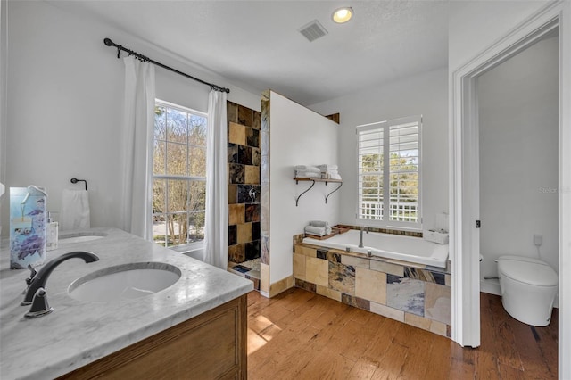 full bathroom featuring visible vents, a sink, wood finished floors, tiled shower, and a bath