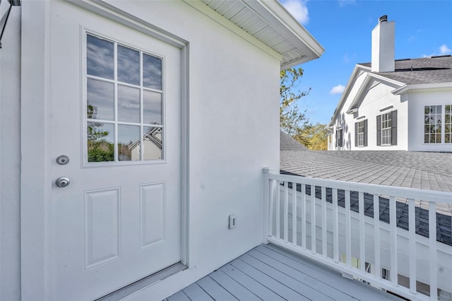 entrance to property featuring a shingled roof and a deck